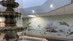A multi-tiered fountain with water cascading down into a pool, surrounded by a mural depicting underwater life.