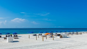 Ein Strand mit Reihen von Liegestühlen und Sonnenschirmen, einem klaren Himmel und dem Meer im Hintergrund.