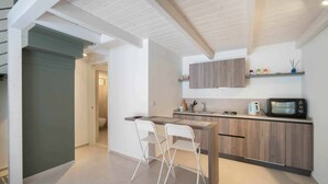 A modern kitchen with a wooden countertop, a built-in microwave, and a sink. There are two white chairs and a small island with a table. - WePuglia - Dimore Stefania - Suite Viuzza (Polignano a Mare)