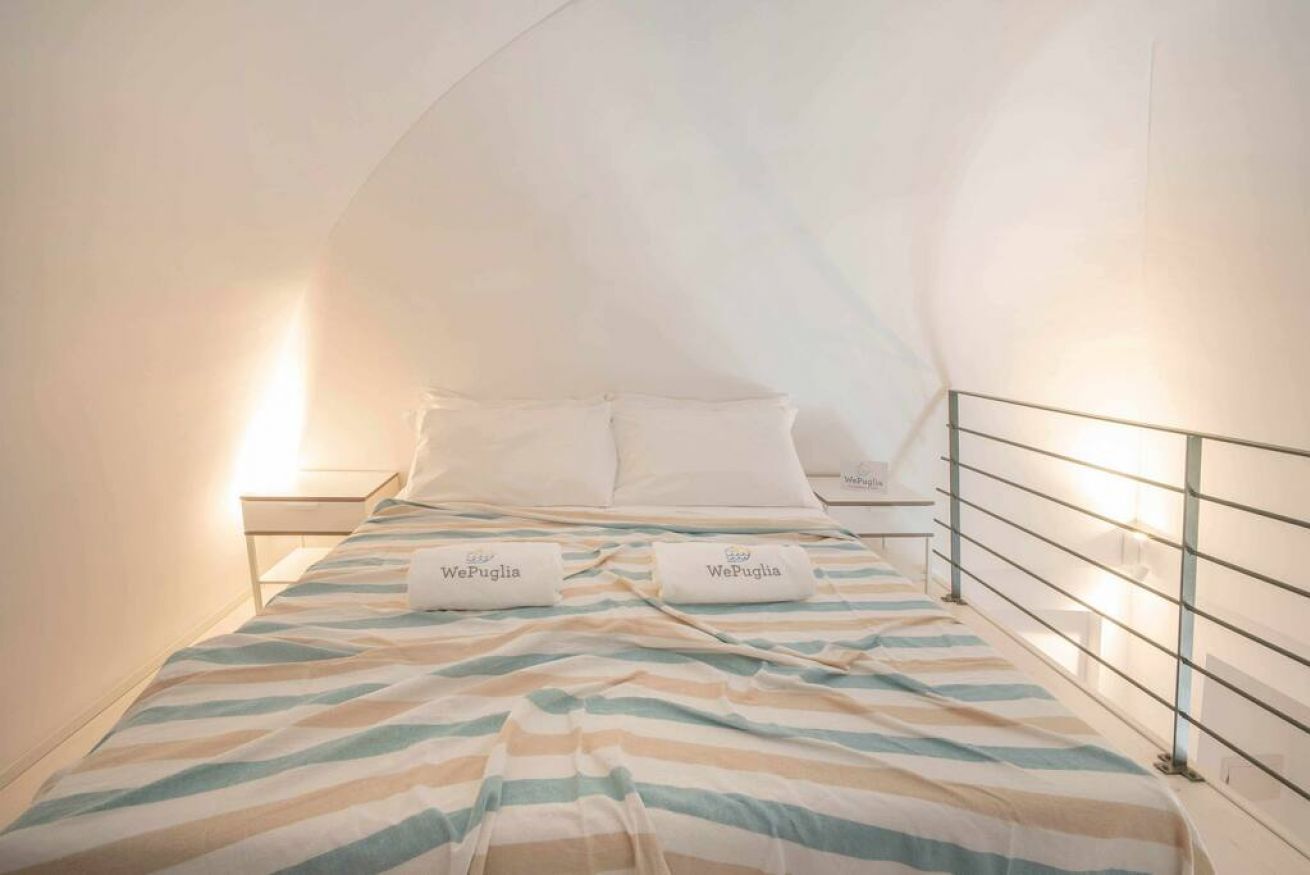 A single bed with striped bedding and two pillows labeled 'WePuglia.'