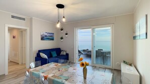 A dining area with a table, chairs, a vase with flowers, a blue sofa, and a view through a glass door.