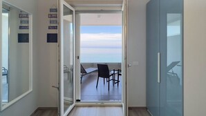 A room with a sliding glass door leading to a balcony with a view of the sea.