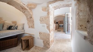 Um quarto rústico com paredes de pedra aparente, um banco de madeira e uma cozinha ao fundo.