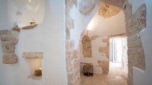 Interior com paredes de pedra, uma pequena janela e uma porta que dá para outro cômodo.