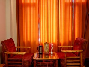 Una habitación con dos sillones tapizados en rojo, una mesita de madera y una cortina a rayas verticales.