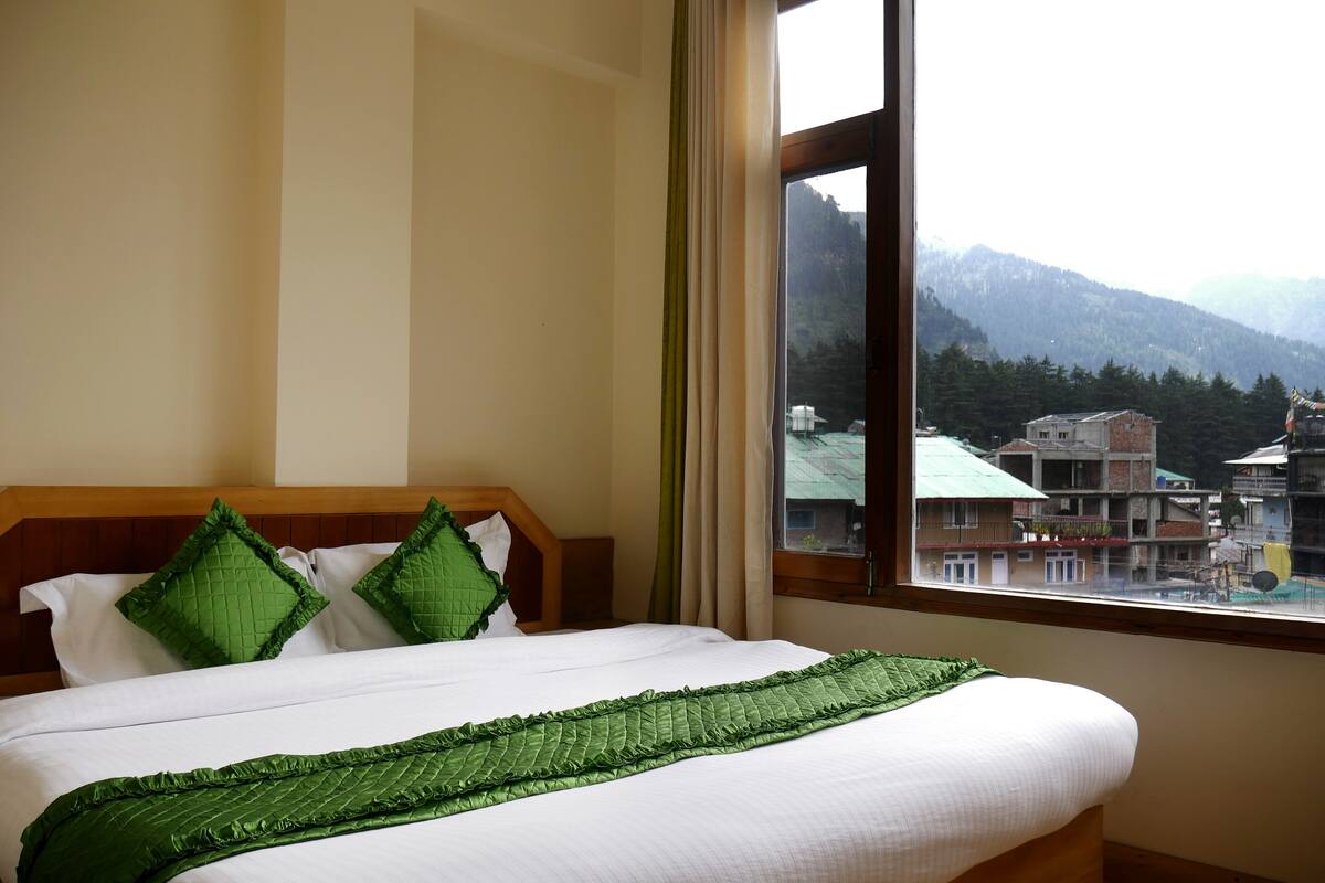 A hotel room with a bed, a view of mountains, and a window with curtains.