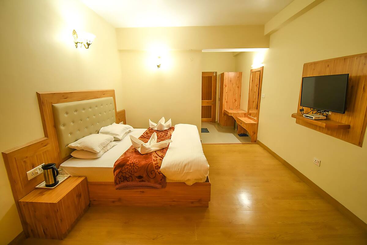 A hotel room with a wooden bed, a television mounted on the wall, and a small bedside table with a coffee maker.