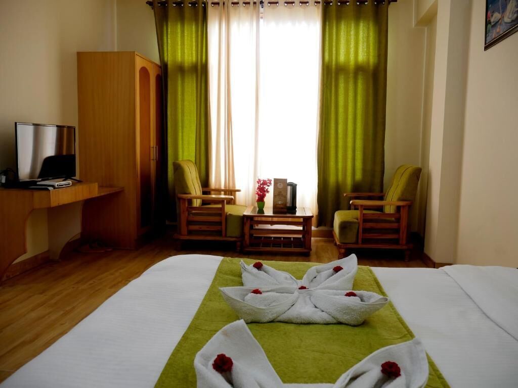 A hotel room with a bed, two chairs, a small table, and a TV on a wooden stand.