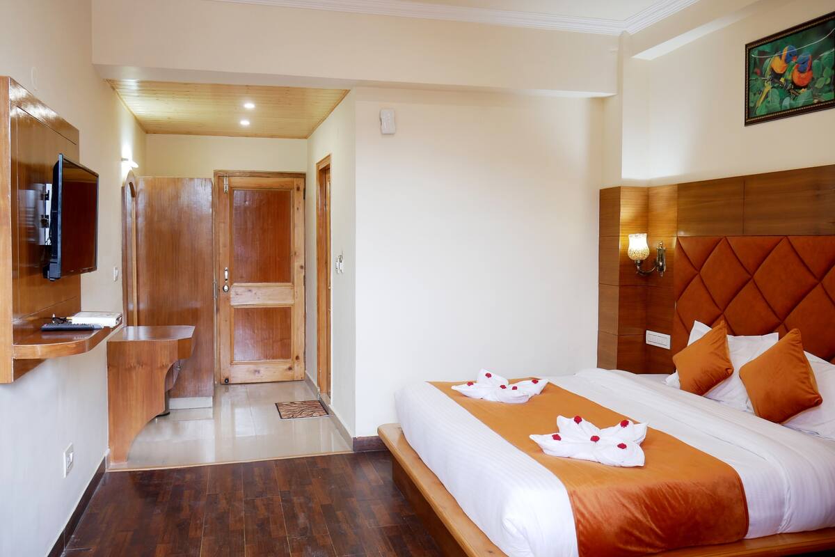 A hotel room with a bed, a TV, a wooden door, and a hallway.