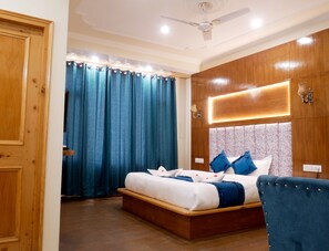 Un dormitorio con una cama de madera, un sillón tapizado azul, un ventilador de techo y una mesita de noche con lámpara.
