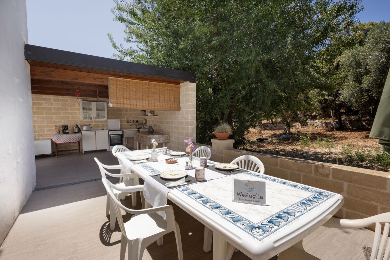An outdoor dining area with a table set for four, surrounded by white chairs, and a sign indicating 'WePuglia'.