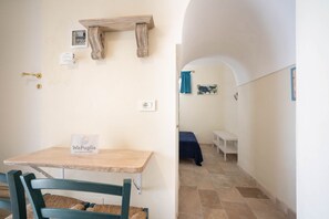 Una habitación con una mesa de madera, una silla, una cama con colcha azul, un estante con una foto y un cartel en la pared.