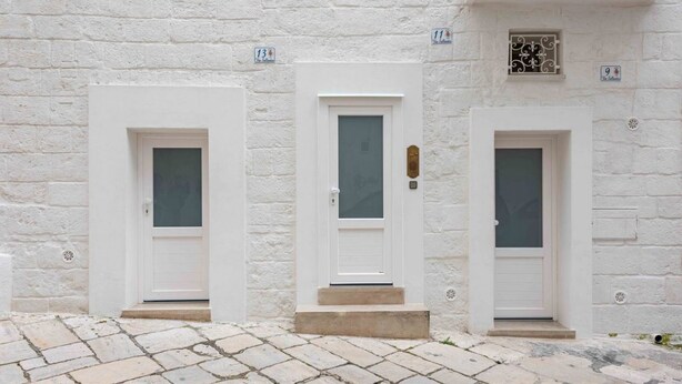 Tres puertas blancas con los números 11, 13 y 9 sobre una pared de piedra blanca.