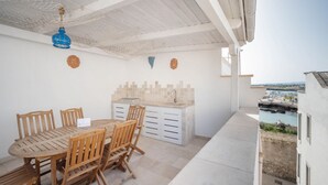 Un patio con una mesa y sillas de madera, un armario blanco y vista al mar.