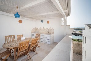 A patio with a wooden table and chairs, a white cabinet, and a view of the sea.