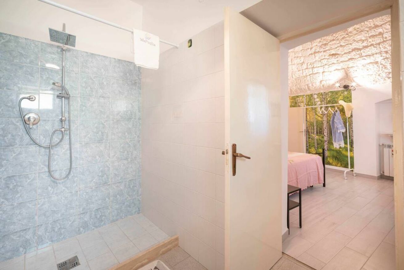 Een badkamer met een douche, een handdoekhouder en een bed in de aangrenzende kamer.