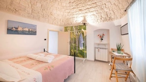 A bedroom with a stone ceiling, a bed with a floral bedspread, a small table with chairs, and a radiator. - WePuglia - La Maison-D B&B - Trullo (Cristo Re)
