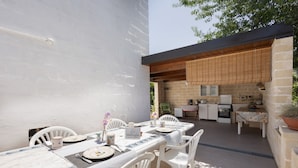 An outdoor dining area with a table set for two, a kitchen in the background, and a stone wall. - WePuglia - La Maison-D B&B - Trullo (Cristo Re)