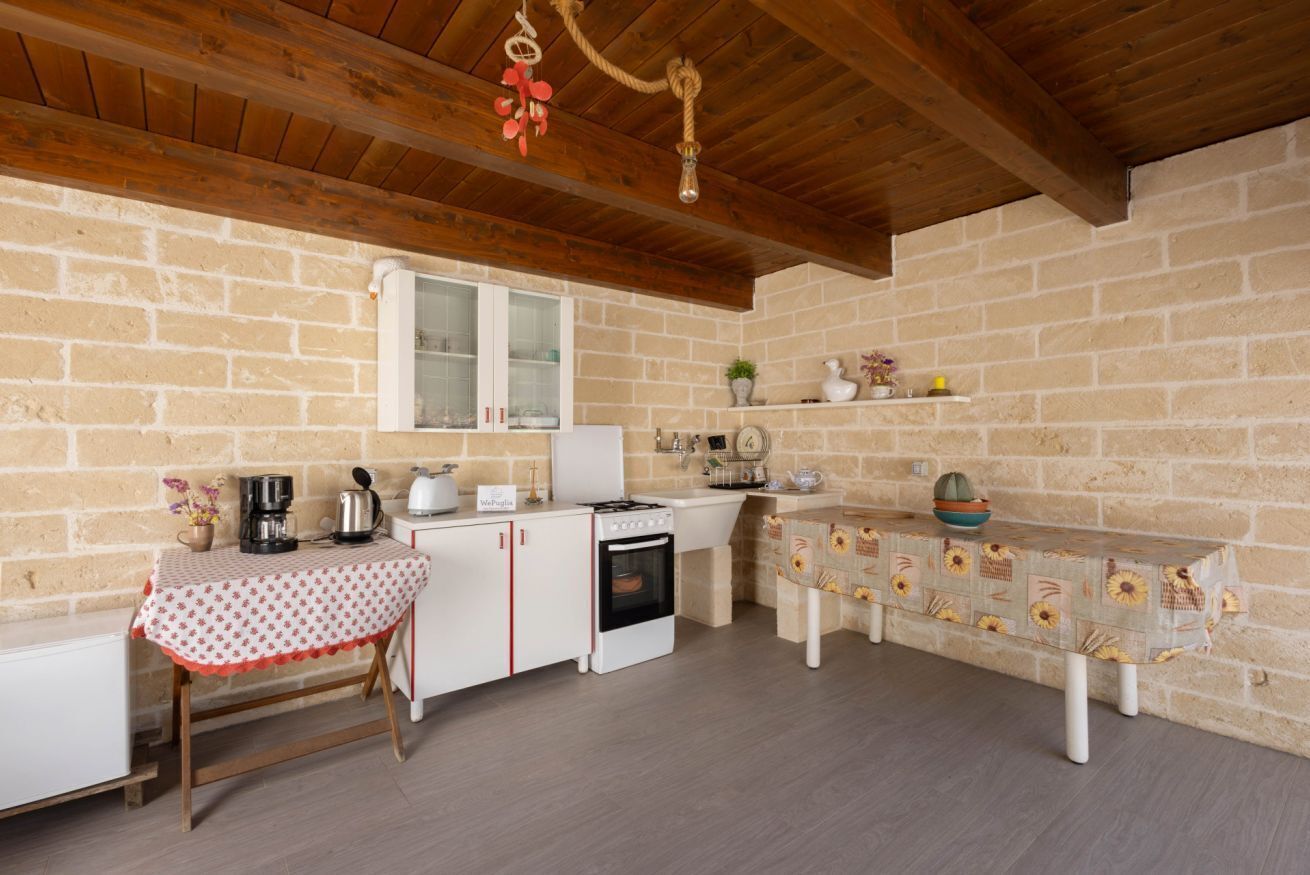 A rustic kitchen with exposed brick walls, wooden beams, a white refrigerator, a stove, and a table with a floral tablecloth.