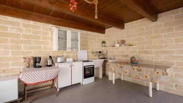 A rustic kitchen with exposed brick walls, wooden beams, a white refrigerator, a stove, and a table with a floral tablecloth.