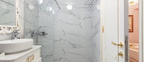 Un baño con ducha de mármol, lavabo con detalles dorados y espejo con marco decorativo.