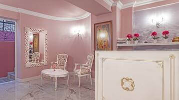 A pink-themed room with a white marble floor, a white table with chairs, a large mirror, and a painting on the wall.