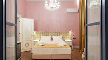 A bedroom with a large bed, a chandelier, a wardrobe, and a bedside table.