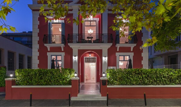 A red building with a central entrance, two balconies, and a well-lit facade. - Via Villa Iliotti (Rhodes)