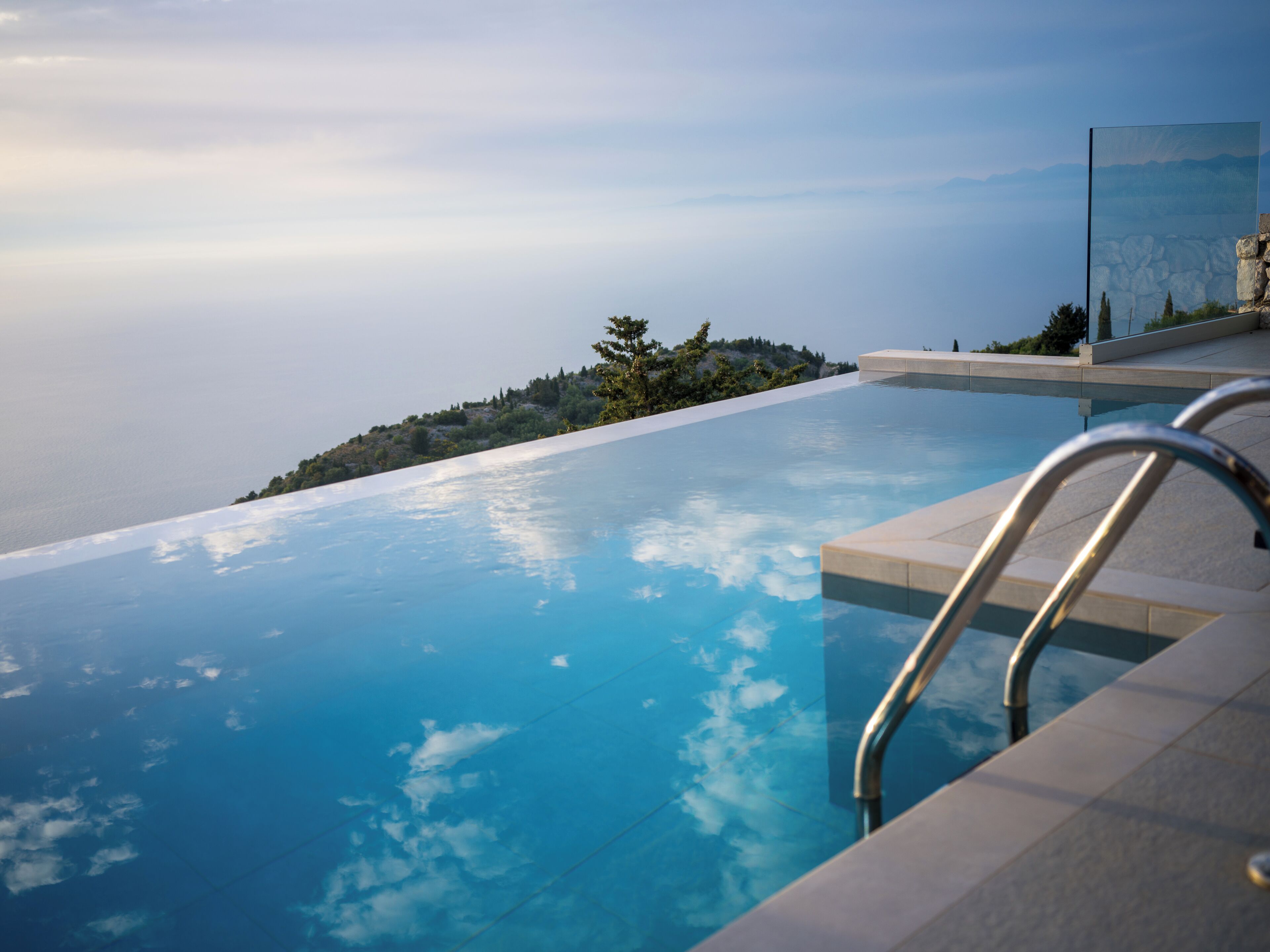 Una piscina infinita con vistas despejadas al océano y una cadena montañosa distante.