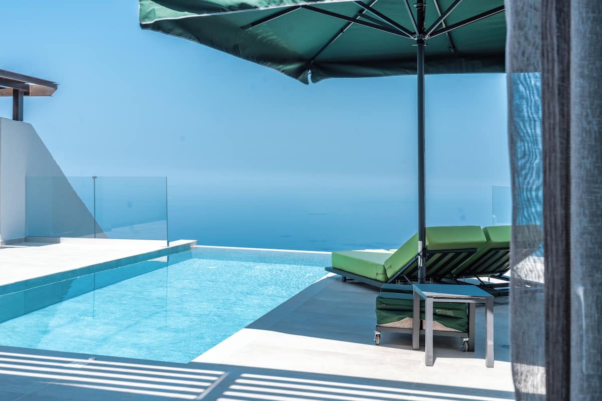 A clear blue sky, a swimming pool, and a green umbrella.
