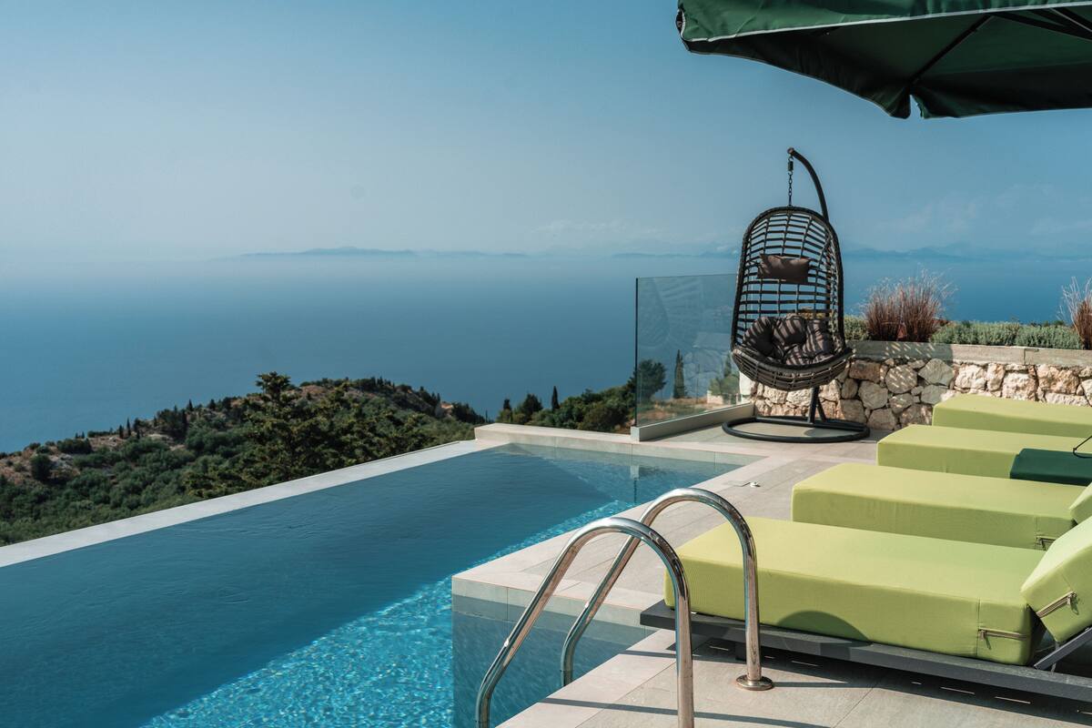 A pool with a clear view of the sea, a stone wall, and a green umbrella.