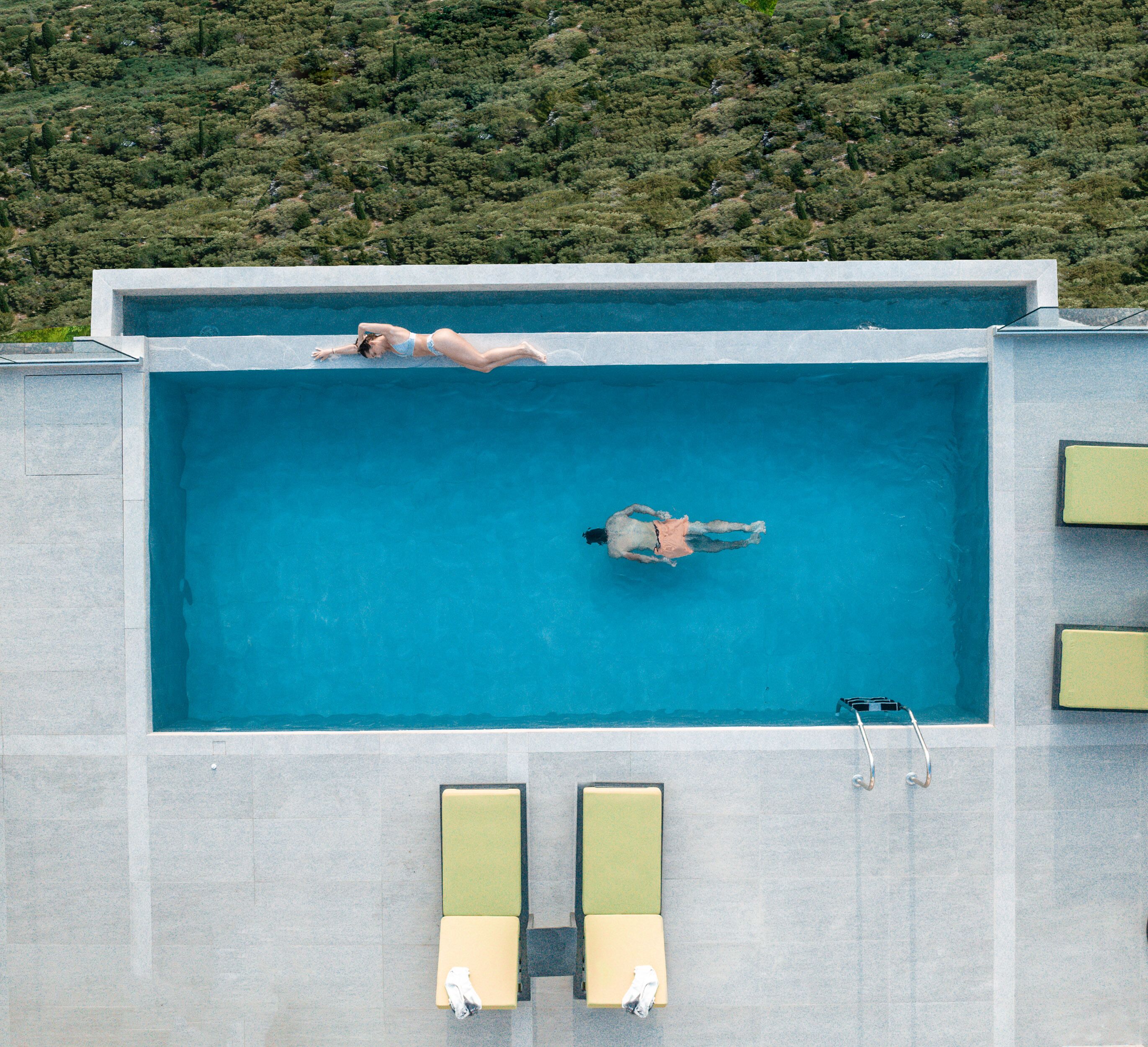An aerial view of a rectangular swimming pool with two lounge chairs and a diving board.