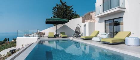 A modern pool area with clear blue water, sun loungers, and a view of the sea.