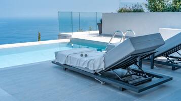 A modern outdoor pool area with two lounge chairs and a glass balustrade overlooking the sea.