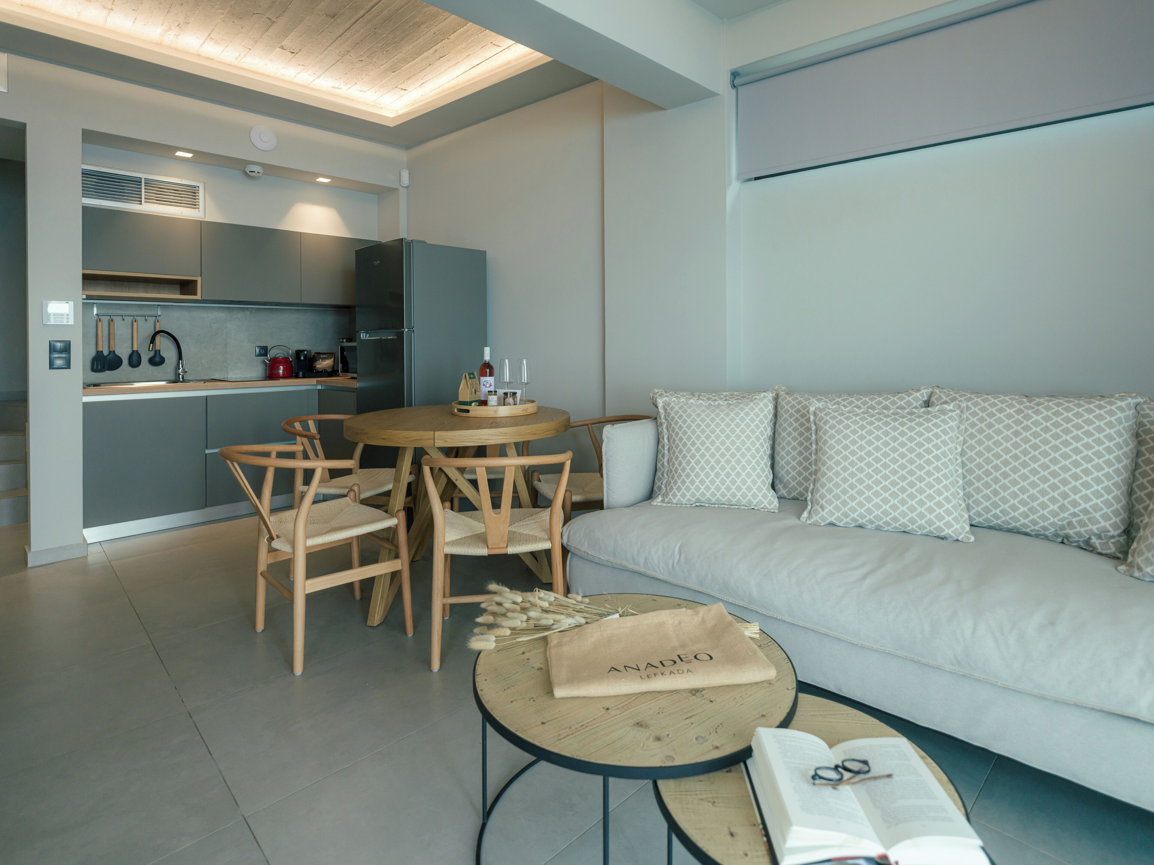 Una sala de estar moderna con un sofá, una mesa redonda de madera y una cocina al fondo.