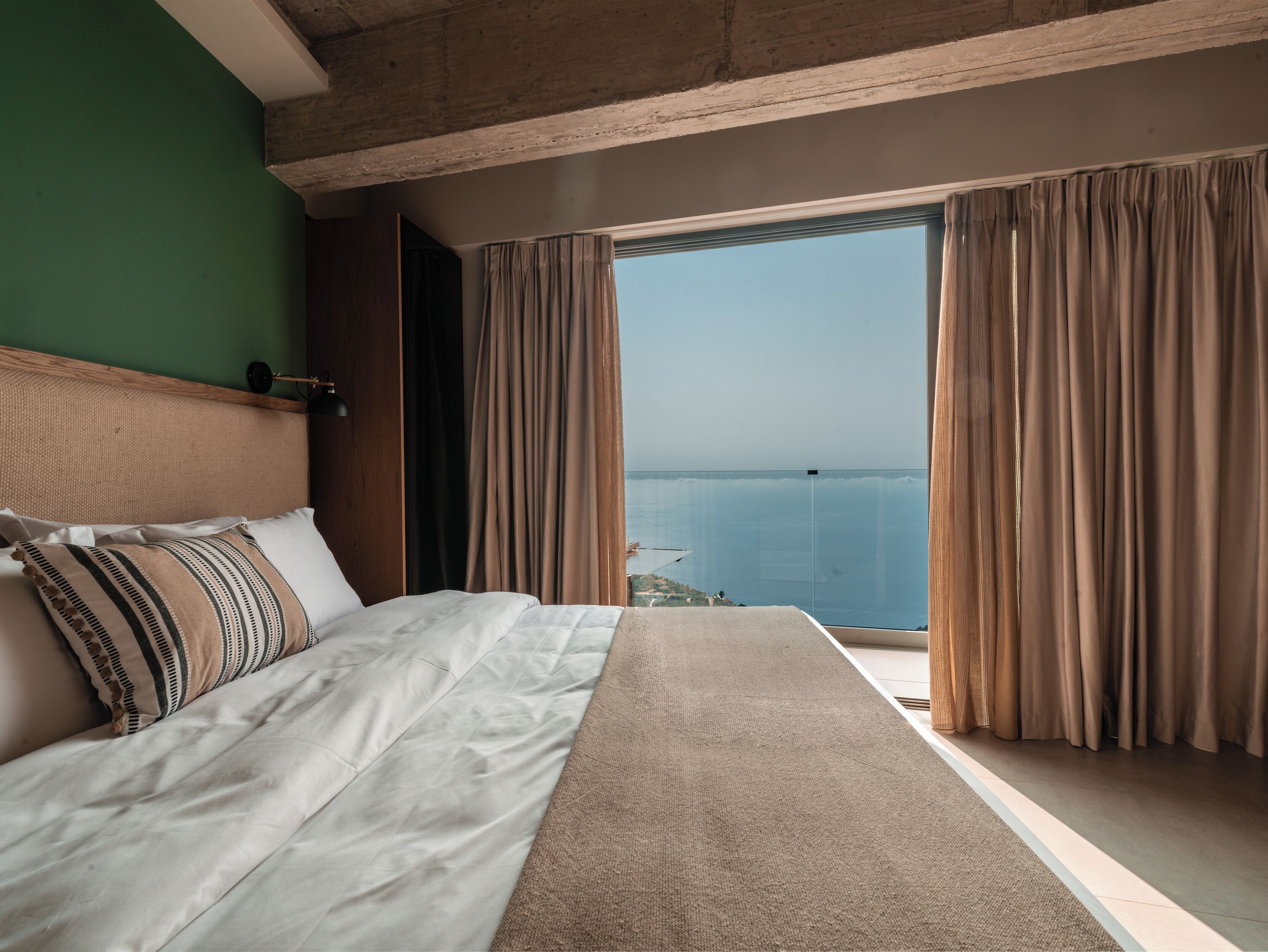 Een slaapkamer met een groot bed, uitzicht op zee en gordijnen.