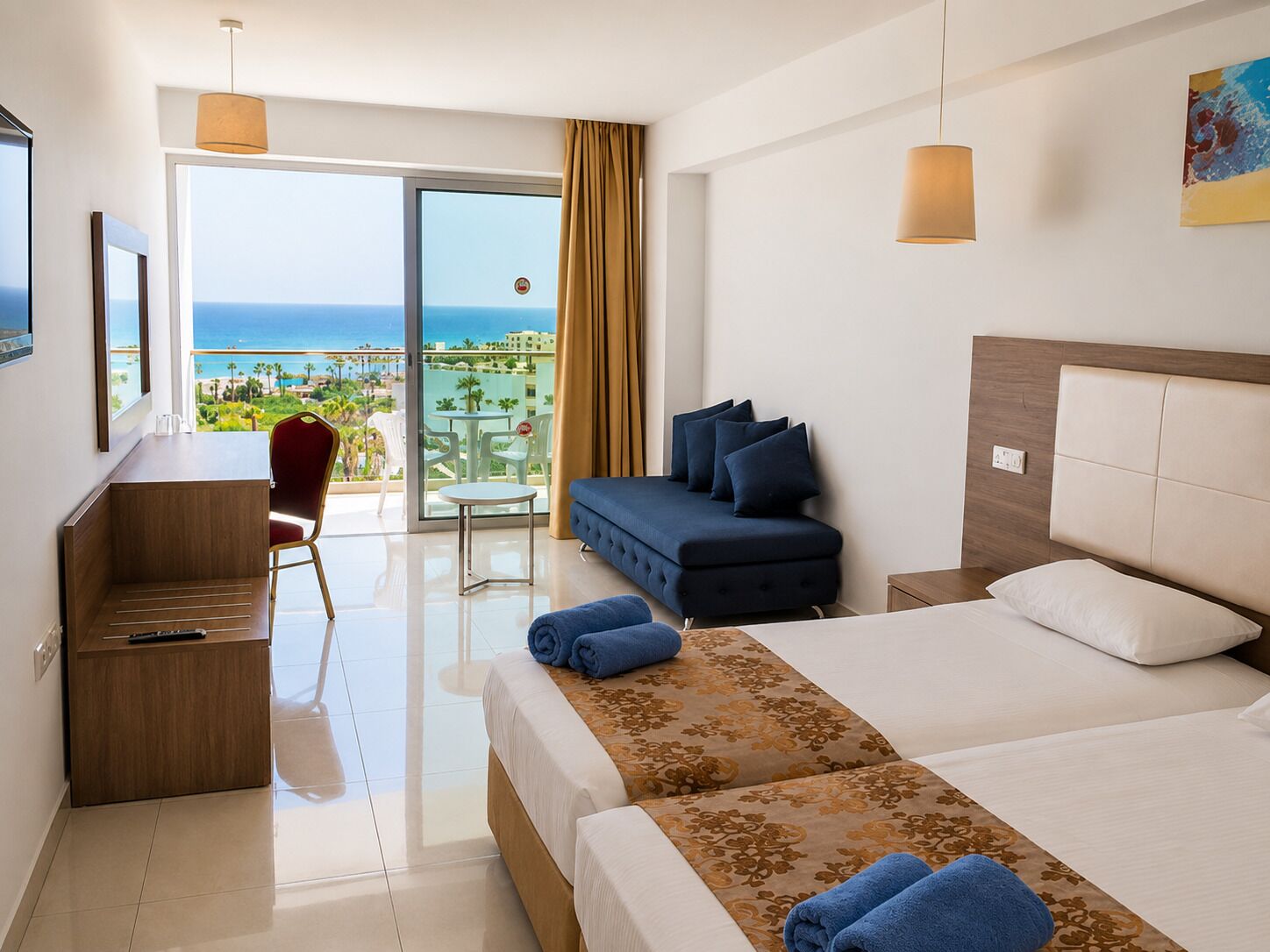 Quarto de hotel com cama, escrivaninha, poltrona, sofá e varanda com vista para o mar.