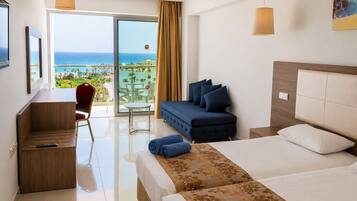 Quarto de hotel com cama, escrivaninha, poltrona, sofá e varanda com vista para o mar.