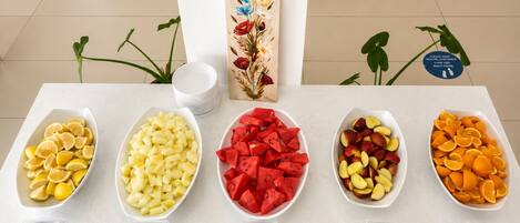 A buffet table with labeled bowls of various fruits including lemons, melon, watermelon, nectarines, and oranges.