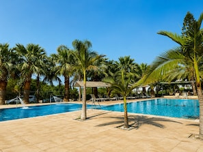 A pool area with palm trees, lounge chairs, and a clear blue sky. - Corfu Hotel (Ayia Napa)