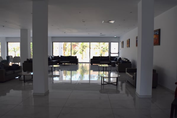 A spacious lobby with a high ceiling, large windows, and a modern seating area with sofas and tables.