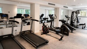 Un gimnasio con varias caminadoras, elípticas y equipo de levantamiento de pesas.