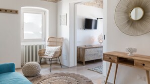 A room with a wicker chair, a wooden desk, a round mirror, and a television mounted on the wall. - Terrazza Ariafina by Wonderful Italy (Ostuni)