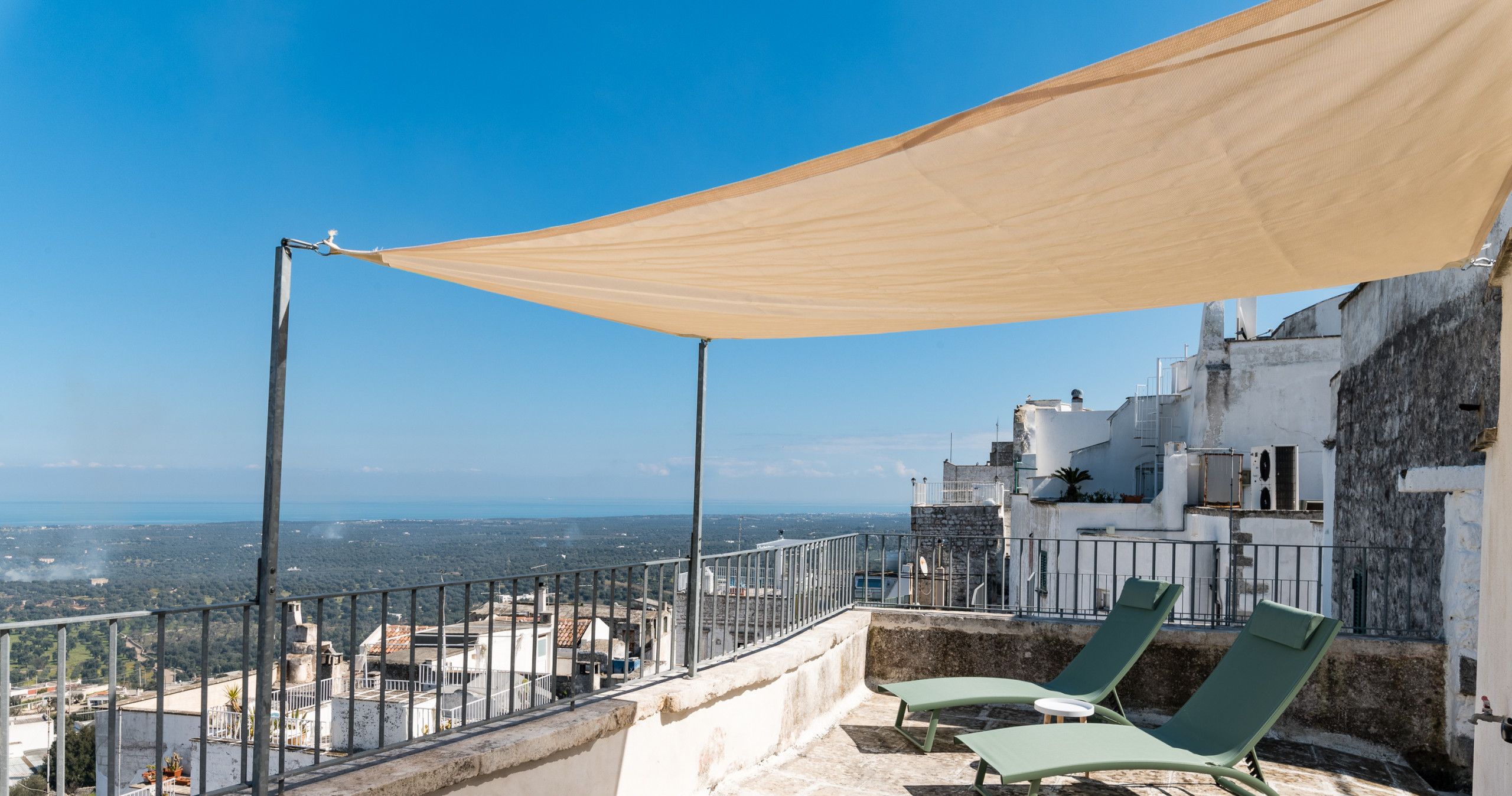 Eine Dachterrasse mit Blick auf die Stadt, zwei Liegestühle und ein großes Sonnensegel.
