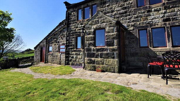 A stone building with multiple windows and a door, a paved pathway, and a chair outside. - Rake Hey Farm (Todmorden)