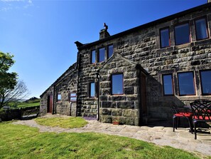 A stone building with multiple windows and a door, a paved pathway, and a chair outside. - Rake Hey Farm (Todmorden)
