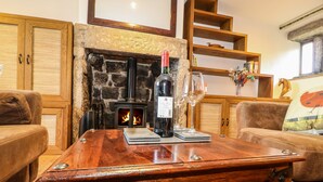 A cozy living room with a stone fireplace, wooden furniture, and a table with a bottle and glasses. - Rake Hey Farm (Todmorden)