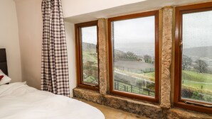 A bedroom with a large bed, a checkered curtain, and three windows overlooking a rural landscape. - Rake Hey Farm (Todmorden)
