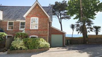 A two-story brick house with a green garage door, a small front garden, and a view of the sea.