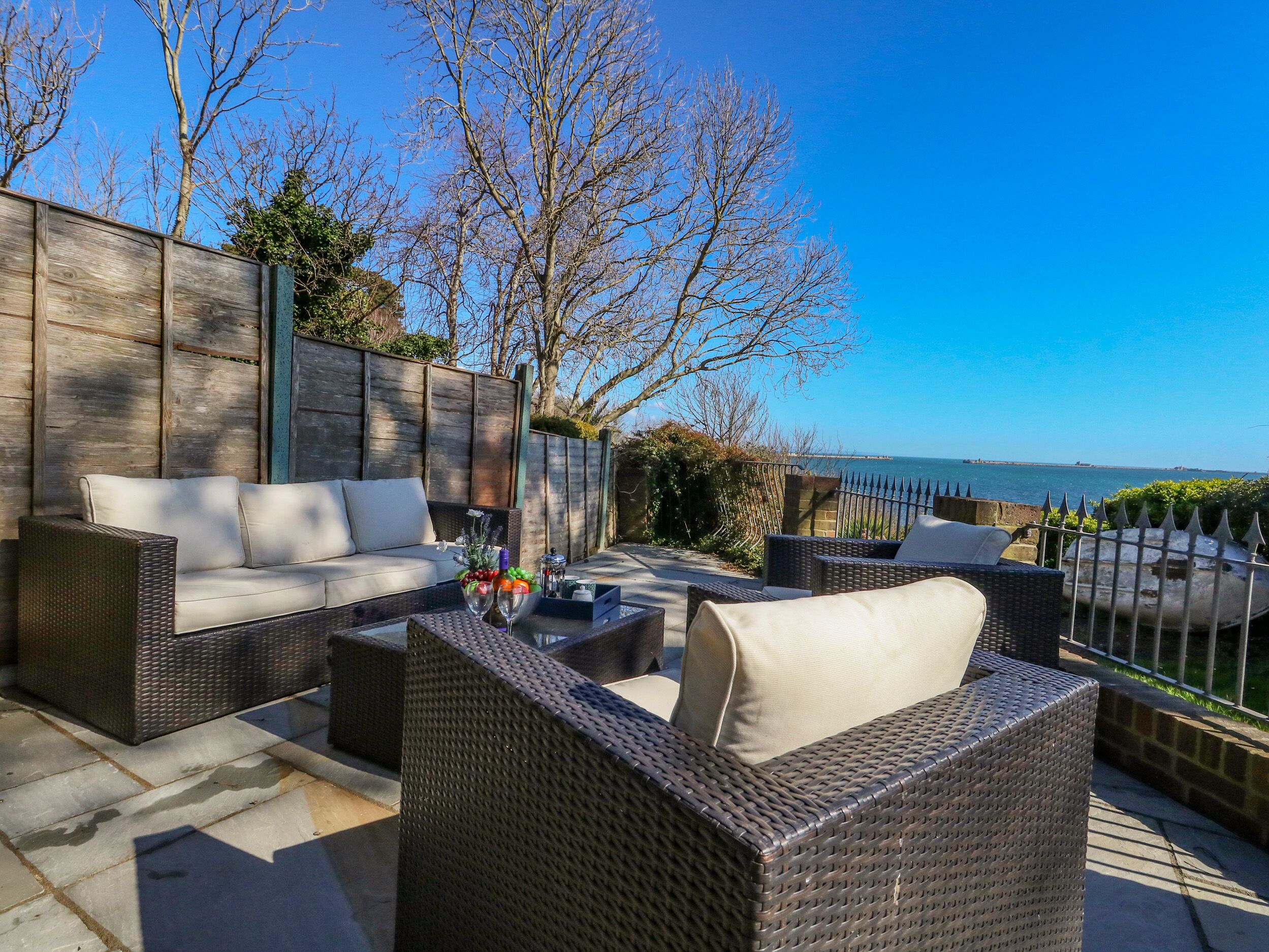 An outdoor seating area with wicker furniture, a glass table, and a view of the sea.